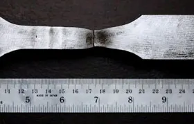 Un échantillon d'essai de traction en métal après avoir été testé jusqu'à la rupture, montrant des preuves claires de fracture ductile et de « rétrécissement » au point de rupture, avec une règle pour l'échelle.