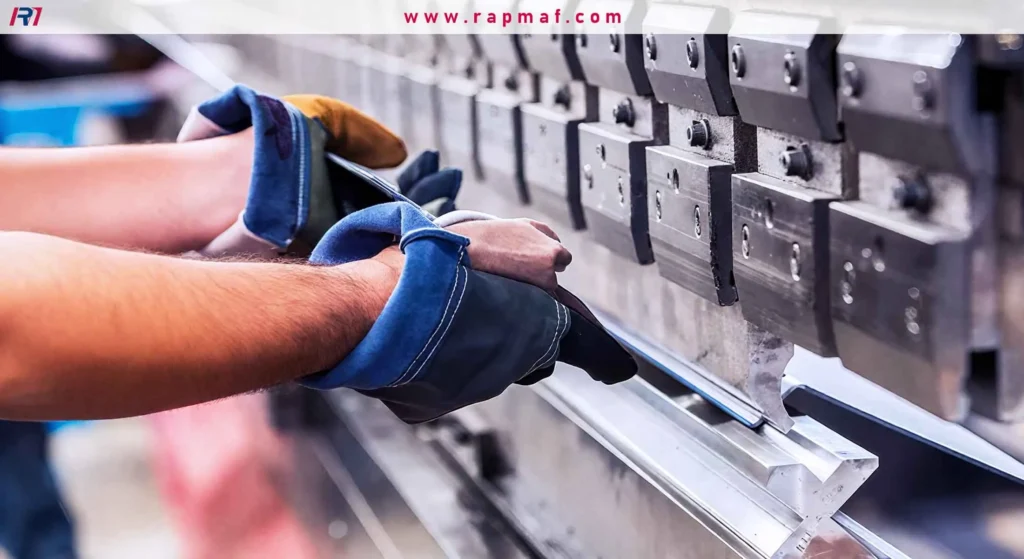 A close-up of a worker's gloved hands carefully guiding a sheet of metal into a press brake machine to be bent into a precise angle.