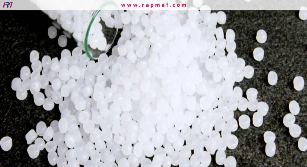 A macro close-up of white, translucent polymer resin pellets, the raw material for plastic manufacturing, spilling onto a dark, textured surface.