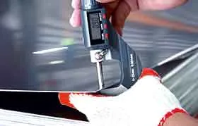 A close-up of a digital micrometer being used to measure the thickness of a steel sheet, with the digital display showing the precise measurement for quality control.