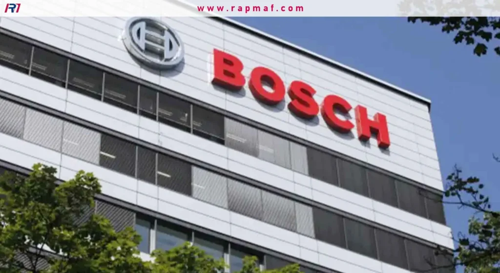The facade of a large, modern Bosch corporate building, featuring the prominent red Bosch logo and emblem above rows of windows, with tree branches in the foreground.