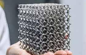 Um close-up de um intrincado componente de metal impresso em 3D com uma estrutura celular ou semelhante a espuma, um excelente exemplo das peças avançadas que podem ser obtidas por meio da manufatura aditiva de metal.
