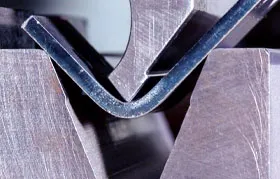 A piece of sheet metal being formed into a right angle by an industrial press brake, a prime example of controlled plastic deformation in manufacturing.