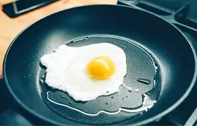 Uma imagem em close-up de um ovo frito deslizando facilmente na superfície de uma frigideira antiaderente, mostrando a superfície de baixo atrito criada pelo revestimento de PTFE.