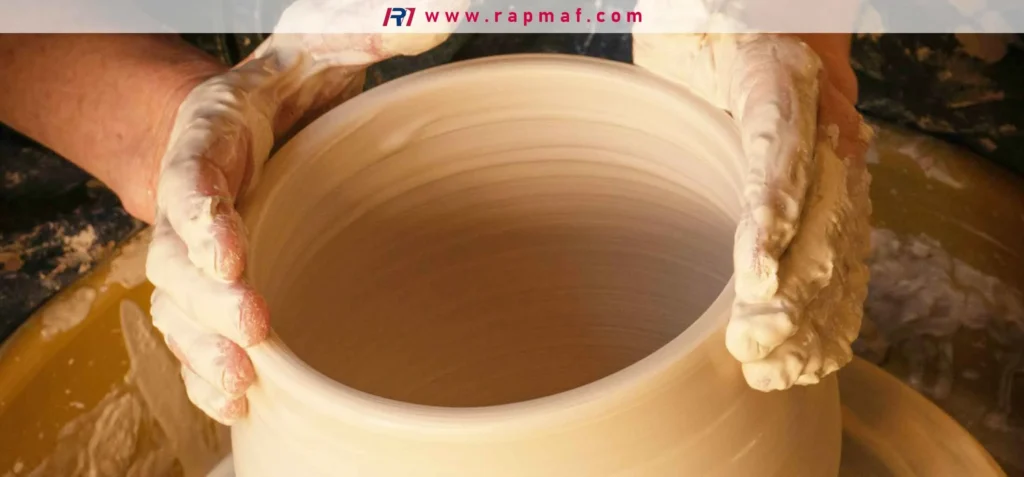The hands of an artisan shaping wet clay into a pot on a potter's wheel, demonstrating the craft of throwing pottery.