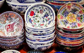 Diversas pilhas de tigelas de cerâmica tradicionais, pintadas à mão, com padrões florais coloridos e intrincados. Isso representa a compreensão comum da cerâmica como louça, em contraste com a cerâmica técnica avançada usada na engenharia.