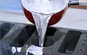 Fundição de alumínio, processo no qual o metal fundido é despejado de uma concha com cabo vermelho em um molde de lingote com múltiplas cavidades para esfriar e solidificar, adquirindo uma forma utilizável.