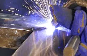 The molten weld pool of a Gas Metal Arc Welding (GMAW) process, characterized by its intense light and heavy spatter, as the consumable electrode fuses the base metals.