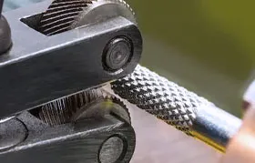 Uma imagem ampliada de uma ferramenta de recartilhamento tipo tesoura, onde duas rodas de recartilhamento opostas aplicam pressão em uma peça de trabalho, formando a frio um padrão de diamante preciso através da deformação plástica do material da superfície.