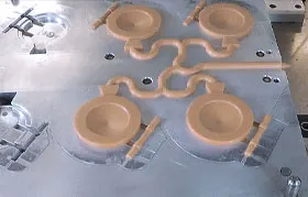 The core side of an injection mold after a cycle, displaying the finished plastic parts, the runner, and the gates before ejection. The image shows a multi-cavity mold designed for high-volume manufacturing.