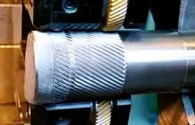 A pair of knurling wheels on a lathe creating a diagonal (helical) grip pattern on a metal shaft.