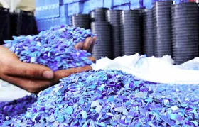 A person's hands holding a scoop of blue polypropylene regrind or pellets. These raw materials are ready to be fed into an injection molding machine to produce new plastic parts, illustrating a key step in the polymer manufacturing supply chain.