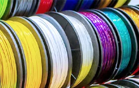 A rack displaying various spools of thermoplastic filament, a common raw material for additive manufacturing. ABS filament, shown here, is popular for its strength but requires proper ventilation due to off-gassing during extrusion.