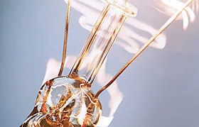 A macro photograph of a coiled-coil tungsten filament heated to incandescence by electrical current. This showcases tungsten's unique combination of high resistivity and the highest melting point of any metal, which made it ideal for early lighting.