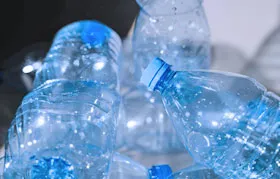 Gambar dekat longgokan botol air plastik kosong dan jernih diperbuat daripada PET (Polyethylene Terephthalate). Imej itu menyerlahkan penggunaan PET yang paling biasa dan berfungsi sebagai pengenalan kepada perbincangan tentang potensi ketoksikan dan keselamatannya.