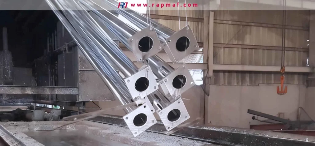 A Rapmaf image showing the industrial hot-dip galvanizing process. A batch of steel light poles are being lifted from a bath of molten zinc, receiving a durable, sacrificial coating for long-term corrosion protection. 