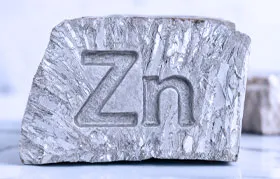 Gambar dekat sekeping logam zink mentah dengan tekstur kristal yang berbeza. Simbol kimia untuk zink, 'Zn', diukir pada permukaannya, mewakili unsur tulen.