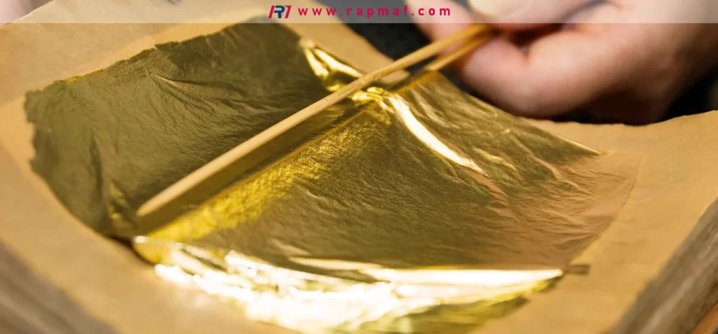 A Rapmaf image showing a close-up of a craftsperson handling an extremely thin sheet of gold leaf with bamboo tweezers, a perfect illustration of the metallic property of malleability, the ability to be hammered into thin sheets without breaking.