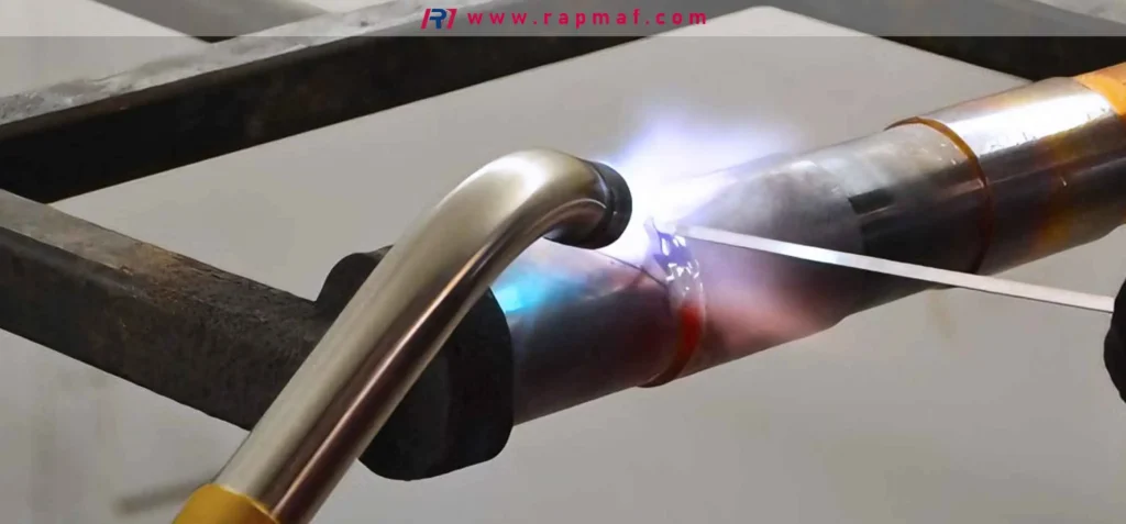 A Rapmaf image of a professional welder performing a precision TIG (Gas Tungsten Arc Welding) weld on a metal pipe. The bright arc is visible as a filler rod is carefully fed into the molten weld pool, all protected by an invisible shielding gas.