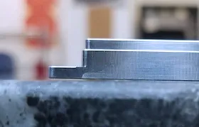 Uma imagem em close-up de uma peça de alumínio usinada com precisão por CNC sendo inspecionada sobre uma placa de granito. Esta vista destaca as superfícies perfeitamente planas e retas que só podem ser obtidas controlando as tensões internas com um tratamento térmico adequado para evitar deformações após a usinagem.