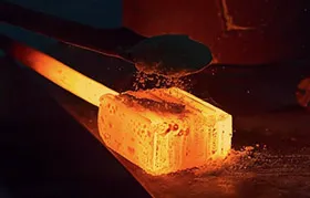 A glowing hot metal block being treated with a carbon-rich powder, illustrating the pack carburizing method of case hardening, a surface heat treatment process.