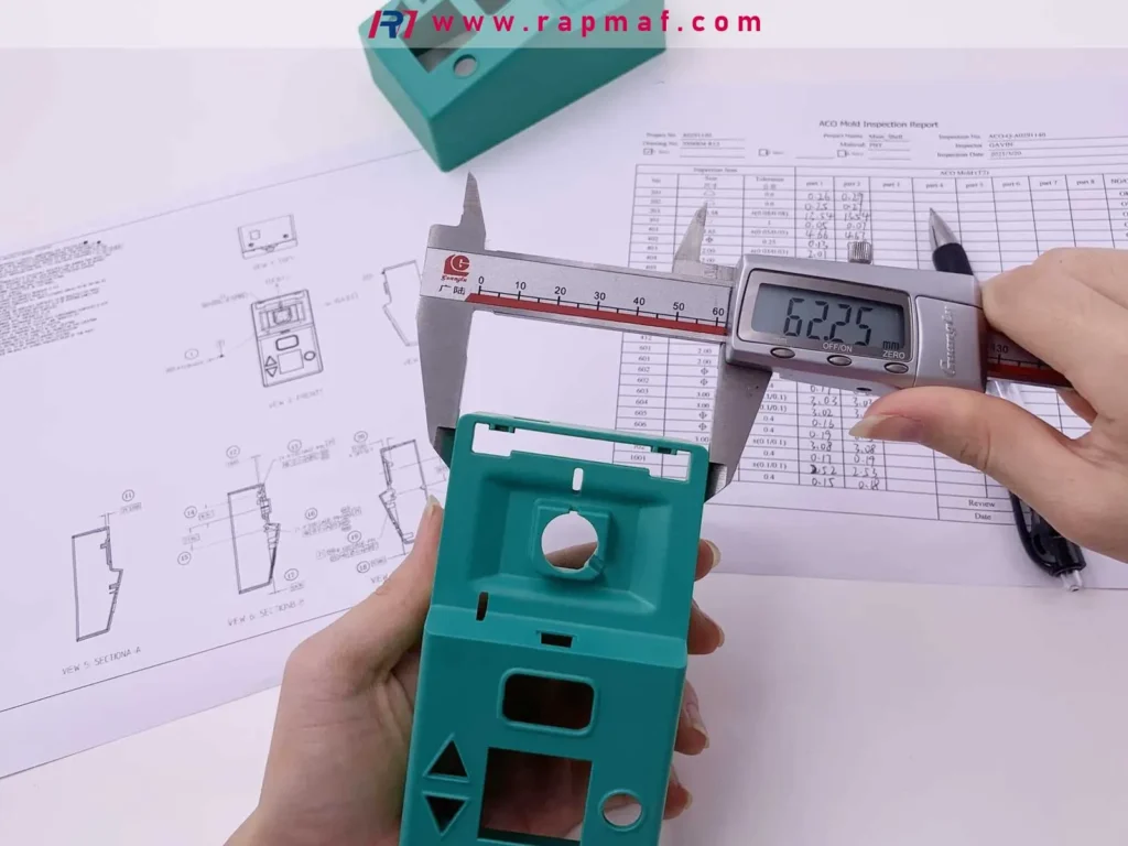 A quality control inspector at Rapmaf meticulously measuring a green plastic molded part with digital calipers, cross-referencing the measurement with the GD&T engineering drawing and an inspection report.