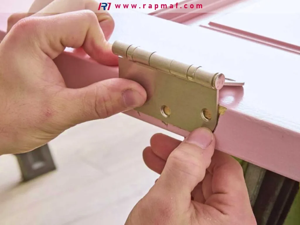 A close-up of a person carefully aligning a brass door hinge before fastening it, a step where pre-drilling pilot holes is crucial for precise alignment and strong screw grip in the wood.