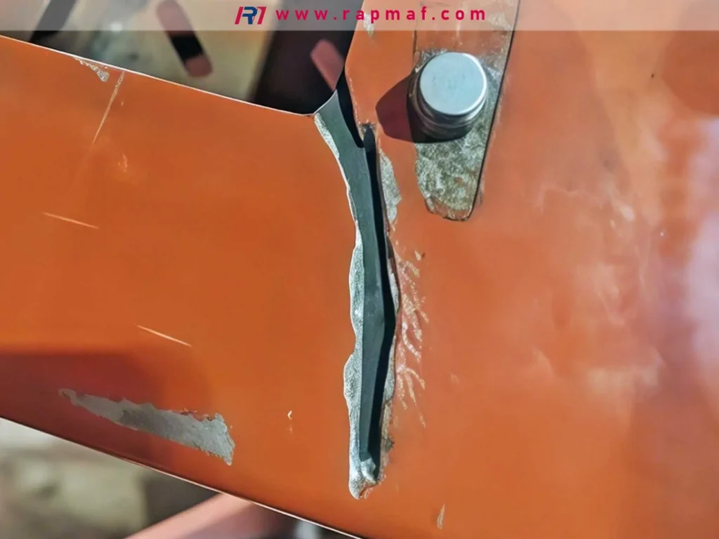A photograph showing a thick, orange-painted metal bracket that has fractured and ripped apart, likely due to a force pulling it beyond its tensile strength limit.