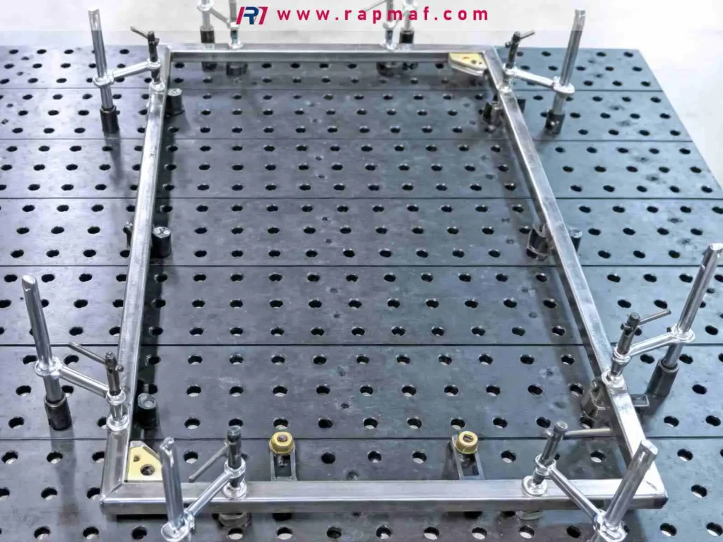 A custom metal frame securely held in a precision welding fixture on a modular jig table, ensuring dimensional accuracy for a complex assembly made from CNC machined components.