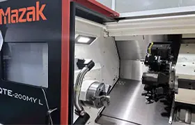 The interior of a Mazak QTE-200MY L CNC turning center at the Rapmaf facility, showing the chuck, tool turret, and brightly lit workspace for high-precision parts manufacturing.