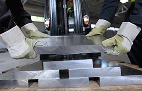 Trabajadores industriales con guantes de seguridad maniobrando una placa de aluminio pesada y gruesa, una materia prima que requiere tanto resistencia como dureza para aplicaciones de fabricación.
