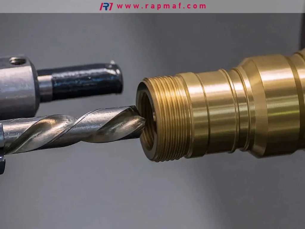 A macro photograph of a high-speed steel drill bit precisely aligned to begin a drilling operation on a custom-machined brass fitting, a basic metalworking cutting process.
