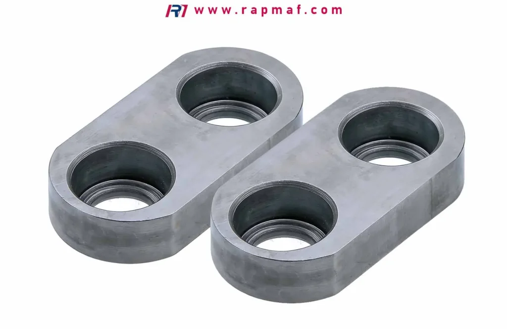 A pair of custom CNC machined steel blocks with an oblong shape, each featuring two precision threaded and countersunk holes. Manufactured by Rapmaf, these parts exemplify the high-quality results of fundamental metalworking operations like milling and drilling.
