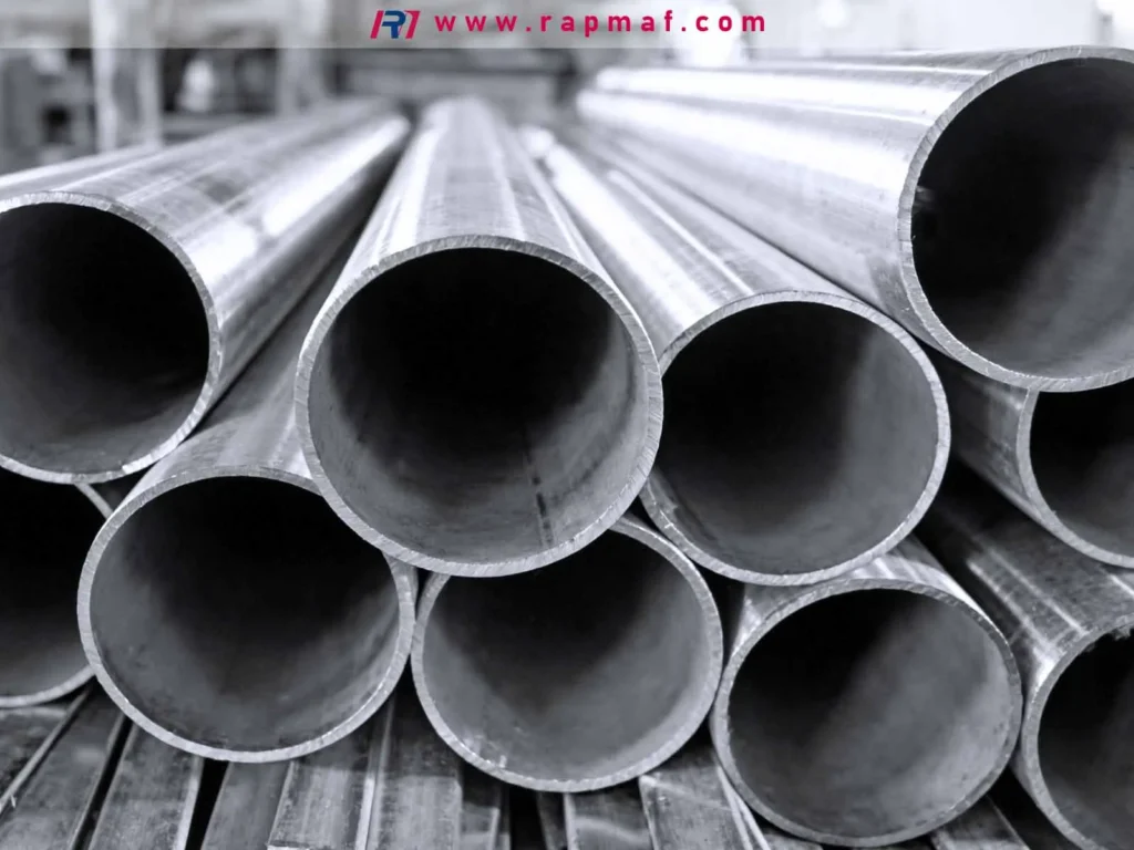 A black and white close-up of stacked, round aluminum pipes, used as the featured image for an article by Rapmaf discussing the cost of aluminum sheet stock. The image sets an industrial tone, highlighting the raw materials used in precision manufacturing.
