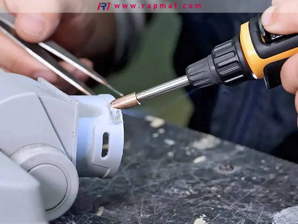 A precision repair of a plastic part using a hot iron to embed a metal mesh reinforcement, demonstrating a technique for strengthening cracked or damaged plastic components.