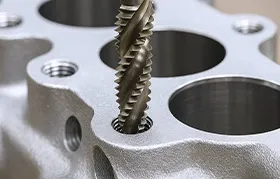 A close-up of a spiral flute tap cutting internal threads into a CNC machined aluminum part, a precision process that is distinct from reaming, which finishes a hole's diameter.