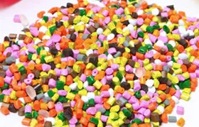 A close-up of a large pile of colorful plastic pellets, the raw material used in injection molding and extrusion, showcasing various pigments like pink, yellow, green, and orange added to the polymer resin.