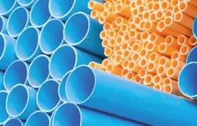 A photograph showing stacks of large-diameter blue PVC water pipes in the foreground with a bundle of smaller-diameter orange PVC electrical conduit pipes in the background, illustrating the material's wide range of applications.