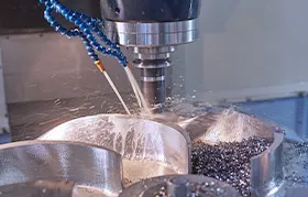 A close-up of a CNC milling machine in operation, with a stream of coolant spraying onto a metal part as the cutting tool removes material and creates chips.