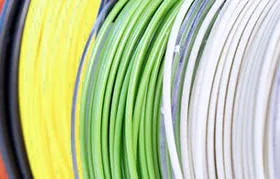 A close-up of several spools of colorful 3D printer filament, including yellow, green, and white PLA, used in Fused Deposition Modeling (FDM) additive manufacturing.
