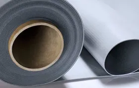 A close-up photograph from Rapmaf of large rolls of grey and white Thermoplastic Polyolefin (TPO) single-ply roofing membrane, the raw material used for commercial roofing.