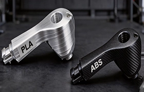 A direct comparison from Rapmaf of two 3D-printed parts, one made from PLA with a metallic finish and the other from a carbon-fiber-textured ABS, illustrating the visual and material differences for engineering prototypes.